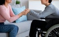 Handicapped teenage boy in wheelchair receiving support from his mother or caregiver, holding her hands at home, closeup