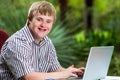 Handicapped young man typing on laptop in garden.