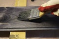 Handling a woody pine plank with a dark mordant with a paintbrush for deeply impregnating wood for painting purposes.