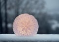 Handmade candlelight made of ice sculpture with white knitted napkin and a candle behind in snowy evening garden.