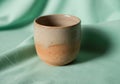 A handmade ceramic cup sits on a soft green fabric background. Royalty Free Stock Photo