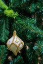 Handmade Christmas tree toy in the form of a white drop, trimmed with gold and brocade on a green artificial spruce. Close