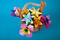 Handmade colored paper flowers origami bouquet paper craft art in a basket with grass in the studio on colored aqua