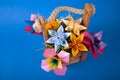 Handmade colored paper flowers origami bouquet paper craft art in a basket with grass in the studio on colored blue