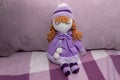 Handmade doll in purple hat and dress on sofa in room.