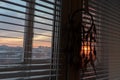 Handmade dreamcatcher hanging by the window with blinds in sunset twilight. Black silhouette of traditional magic amulet for dream