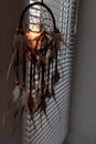 Handmade dreamcatcher hanging by the window with blinds in sunset twilight. Black silhouette of traditional magic amulet for dream