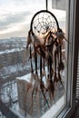 Handmade dreamcatcher hanging by the window in sunrise twilight. Urban city landscape on dackground. Black silhouette of
