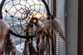 Handmade dreamcatcher hanging by the window in sunrise twilight. Urban city landscape on dackground. Black silhouette of