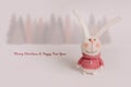 Handmade knitted bunnies stand against a white background. Behind is a forest of fir trees.