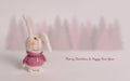 Handmade knitted bunnies stand against a white background. Behind is a forest of fir trees.