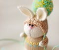 Handmade knitted toy. Easter Bunny with glasses in beige sweater and hat with big pompom close up