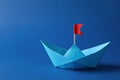 Handmade paper boat with red flag on blue background. Space for text. Origami art Royalty Free Stock Photo