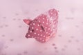 Handmade pink pig with white polka dots and skirt stands on white pink background with snowflakes