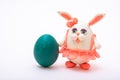 Handmade plasticine Easter bunny in a pink skirt next to a painted Easter green egg on a white background