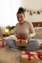 Handmade presents. Happy black lady wrapping gift boxes, making bow using red ribbon tape rope, sitting on bed Royalty Free Stock Photo