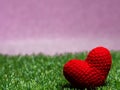 Handmade red yarn heart on Green grass background is royal pink. Royalty Free Stock Photo