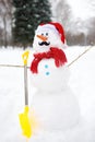 Handmade snowman with a scarf, Santa Claus hat, carrot nose, mustache, hands from branches and shovel in a snowy park Royalty Free Stock Photo