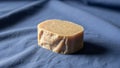 A handmade soap bar rests on a blue fabric surface. The soap is light brown with a rough texture, Royalty Free Stock Photo