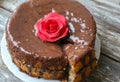 Handmade sponge cake with chocolate frosting. Small cake with cacao ganache glaze. Red sugar rose decorated. Homt pastry. Sweet