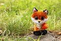 Handmade textile soft toy of a small orange fox with shiny purple eyes and a yellow bead decoration sits on the grass