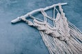 Handmade wall decoration cotton macrame panel on wooden stick over textured blue gray background.