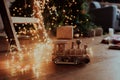 Handmade wooden train in lots of yellow garland, on a dark wooden floor, Christmas tree on the background