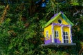 handmade yellow green violet birdhouse hanging on fir tree in garden