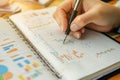 Hands are actively crafting financial plans in a notebook, filled with colorful charts and graphs. The activity suggests Royalty Free Stock Photo