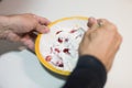 Hands of adult man mixing yoghourt and sliced strawberries