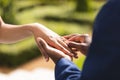 Hands of african american bride and groom placing ring on finger at wedding ceremony in sunny garden