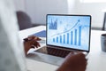 Hands of african american businesswoman at desk using laptop with blue graphs on screen Royalty Free Stock Photo