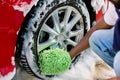 Hands of African man holding green sponge, washing car wheel with foam. Cleaning of modern rims of luxury red car at Royalty Free Stock Photo
