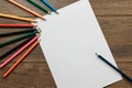 Hands of the artist close-up, holds a pencil over a blank sheet of paper near scattered colored pencils on a brown wooden table. Royalty Free Stock Photo