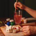 The hands of the artist paint the Easter bunny. Watercolor paints in jars and tubes. Handwork.