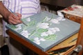 Hands of the artist when painting a picture with flowers