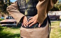 Hands, back pain and paintball with a person standing on a field for military or army training outdoor. War, fitness and