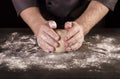 Hands of Baker kneaded dough lump on table with flour, on black