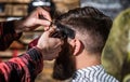 Hands of barber with hair clipper, close up. Bearded man in barbershop. Haircut concept. Man visiting hairstylist in Royalty Free Stock Photo