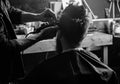 Hands of barber trimming hair of bearded guy with clipper and comb, close up rear view. Hipster client getting hairstyle