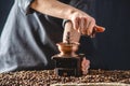 Hands baristas in a dark apron grind on a manual grinder fragrant coffee beans. Selection of fresh coffee for espresso Royalty Free Stock Photo