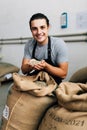 Hands of barrista putting green unroasted coffee beans into sack at factory