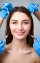 Hands of beauticians holding syringes around flawless woman face ready for injection in cosmetology clinic. Female model Royalty Free Stock Photo