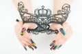 Hands with beautiful manicure holding a black lace carnival mask on white background