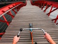 Hands on a Bicycle handlebar POV view. Orange bike on the wooden red Python bridge in Amsterdam, Netherlands Royalty Free Stock Photo