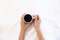 Hands of biracial woman holding cup of coffee sitting in bed at sunny home Royalty Free Stock Photo