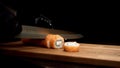 Hands in black gloves cut Philadelphia roll with sharp knife on wooden board, isolated on black background. Salmon and Royalty Free Stock Photo