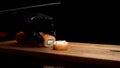 Hands in black gloves cut Philadelphia roll with sharp knife on wooden board, isolated on black background. Salmon and Royalty Free Stock Photo