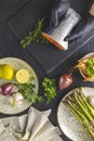 Hands in black gloves support trout fish on black stone cutting board surrounded herbs, onion, garlic, asparagus, shrimp, prawn in Royalty Free Stock Photo