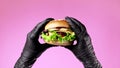 Hands in black latex gloves with burger. Woman holding hamburger. Big appetizing patty with meat cutlet, vegetables
